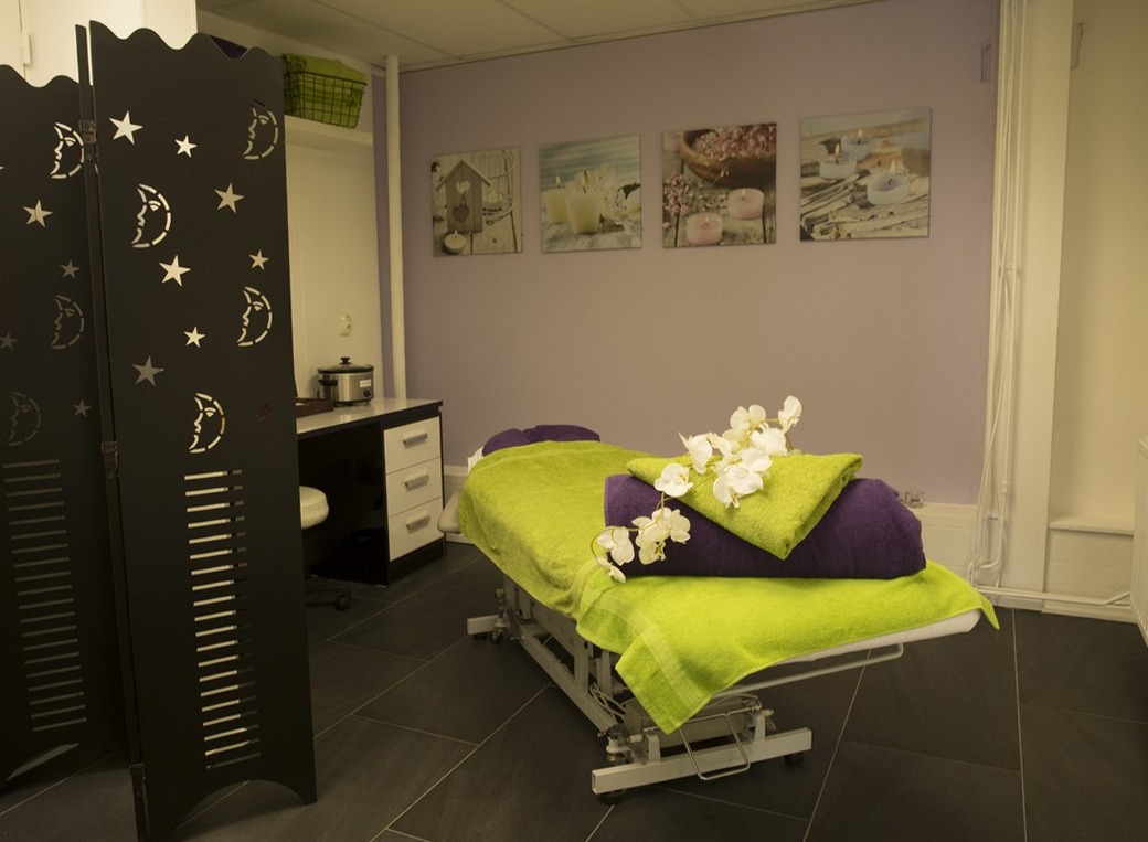 Behandelkamer met een massagetafel, limoengroene doek, orchidee en lila handdoek
