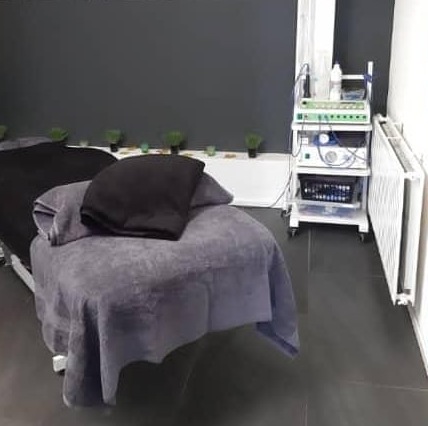 Behandelkamer met een massagetafel onder grijze handdoeken, kleine planten langs een donkere wand en een radiator